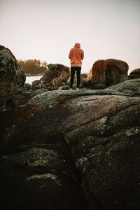 Rear view of man standing on rock against sky