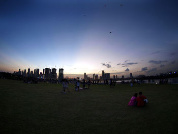 Crowd on grass against sky during sunset