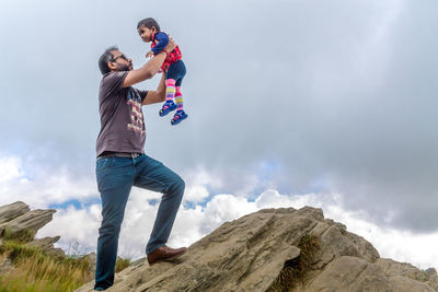Full length of friends standing on rock against sky