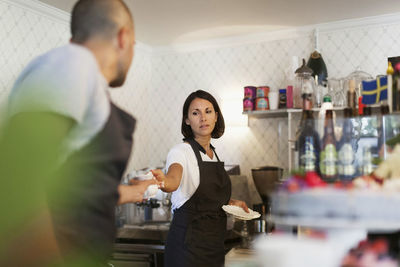 Woman giving cup to male colleague while working at cafe