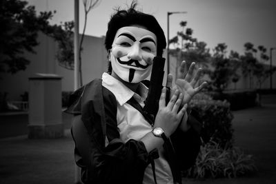 Portrait of a person wearing a mask holding up a fake gun while clapping