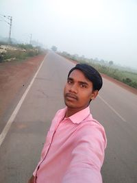 Portrait of young man standing on road against sky