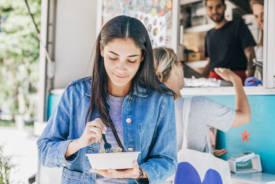 Young woman eating fresh tex-mex in bowl against food truck