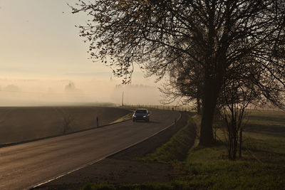 Cars on road by field against sky during sunset