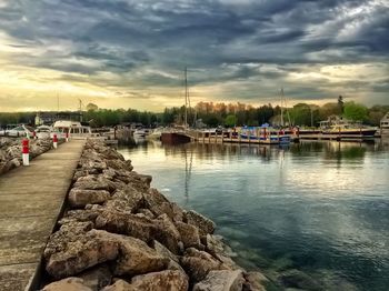 Boats in harbor against cloudy sky