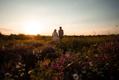 Rear view of couple on field against sky during sunset