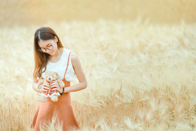 Smiling young woman holding teddy bear while standing on field