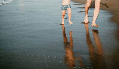 Low section of people walking on wet shore