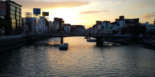 Bridge over river by buildings against sky during sunset