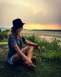 Woman sitting at lakeshore in chitwan national park against sky during sunset