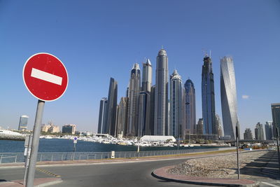 Road sign by modern buildings against clear blue sky