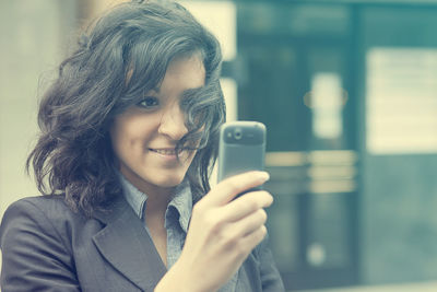 Close-up of smiling young woman using mobile phone in city