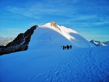 People climbing on snowcapped mountain against sky