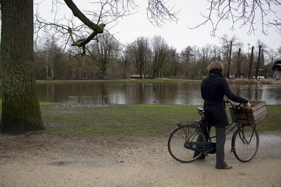 Man riding bicycle by lake against trees