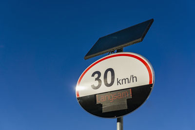 Low angle view of road sign against clear blue sky