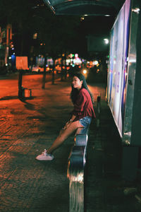 Side view of smiling woman sitting in city at night