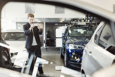 Man photographing car through mobile phone at dealership store