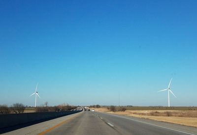 Road by wind turbines against clear blue sky