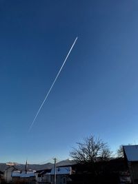 Low angle view of vapor trails over buildings against blue sky