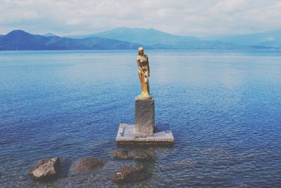 Gold female statue in lake against sky
