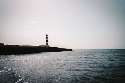 Lighthouse by sea against clear sky