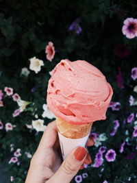 Cropped hand of woman holding ice cream cone against plants