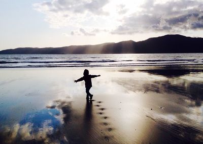 Silhouette boy with arms outstretched playing at beach