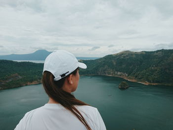 Rear view of woman wearing cap looking at sea amidst mountains