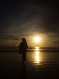 Silhouette woman standing on beach against sky during sunset