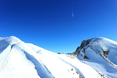 Low angle view of snowcapped mountains against clear blue sky