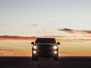 Silhouette of truck at sunrise with headlights and foglight on