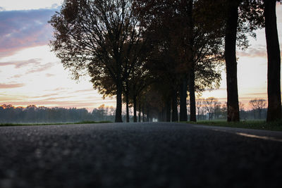 Empty road amidst trees against sky during sunset