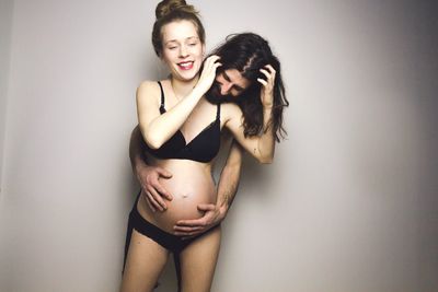 Man embracing pregnant woman standing against gray background