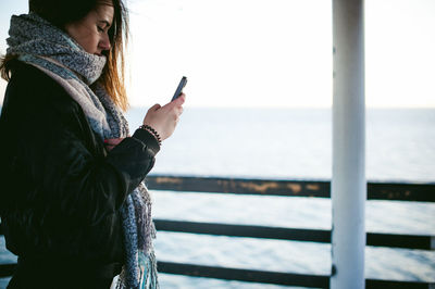 Side view of young woman using phone on pier over sea