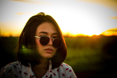 Close-up portrait of young woman wearing sunglasses against orange sky