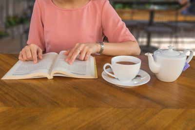 Midsection of woman holding coffee cup on table