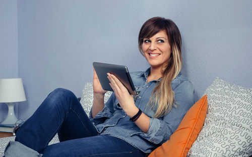 Smiling woman using digital tablet while leaning on bed at home