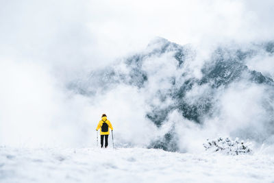 Back view of anonymous hiker with trekking poles walking on snowy ground in pyrenees mountains in andorra