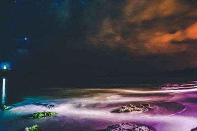 Close-up of hand by sea against sky at night
