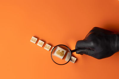 Close-up of hand holding eyeglasses against orange background