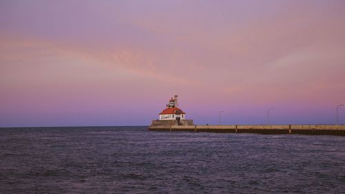 Lighthouse by sea against sky during sunset