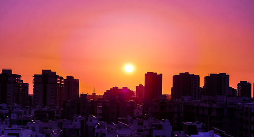 Buildings in city against romantic sky at sunset