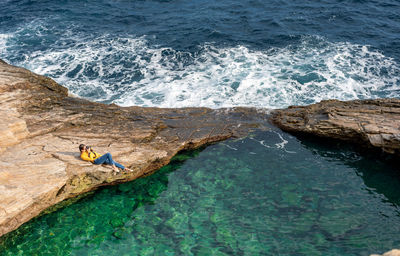 High angle view of woman photographing while relaxing on rocks at beach