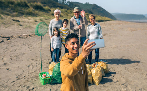 Smiling boy taking selfie with family while standing at beach
