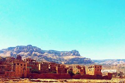 Townscape by mountains against clear blue sky