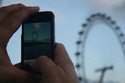 Close-up of hand photographing on mobile phone against sky