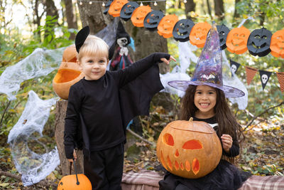 Two kids girl and boy in halloween costume with pumpkins in halloween decorations outdoor