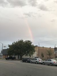 Rainbow over road against cloudy sky