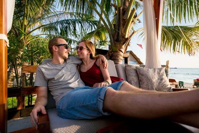 Couple relaxing on chair against palm trees at beach resort