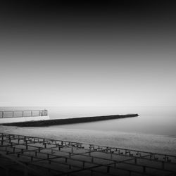 Pier at beach against sky during foggy weather